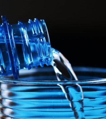 Plastic beverage bottle made from PET preform pouring water into a glass