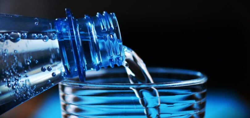 Plastic beverage bottle made from PET preform pouring water into a glass