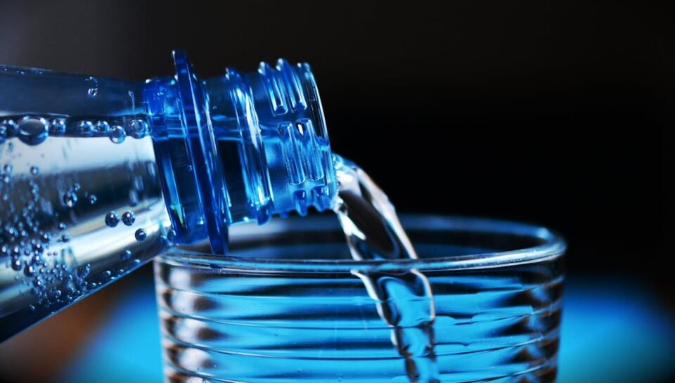 Plastic beverage bottle made from PET preform pouring water into a glass